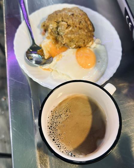Un bolón de verde con huevo frito y una taza de café sobre la barra.